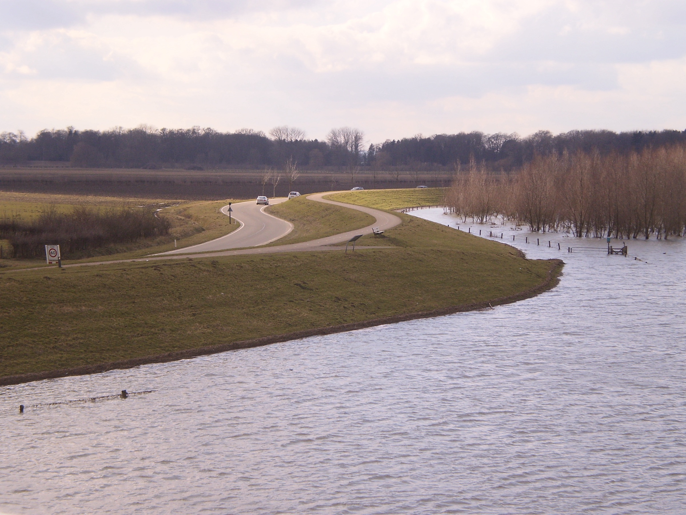 Een slingerende weg over de IJsseldijk bij Deventer, naast hoog water in de uiterwaarden